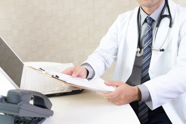 医師がデスクで書類とPCを見る