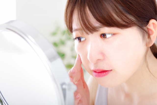 女性が鏡を見ながら頬に触れている様子