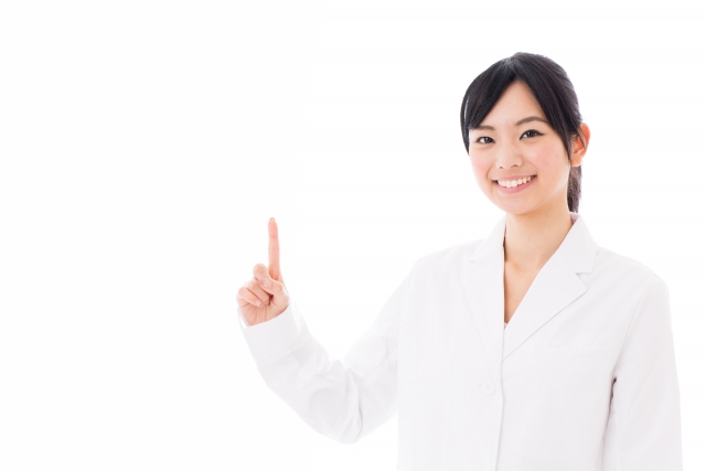 白衣の女性が人差し指を立ててにこやかに笑う