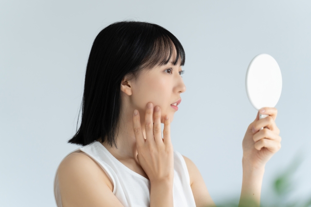 鏡で頬に触れる女性