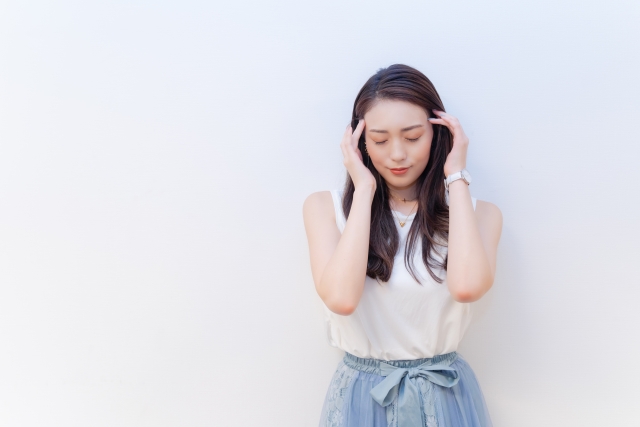 額に触れ悩む女性